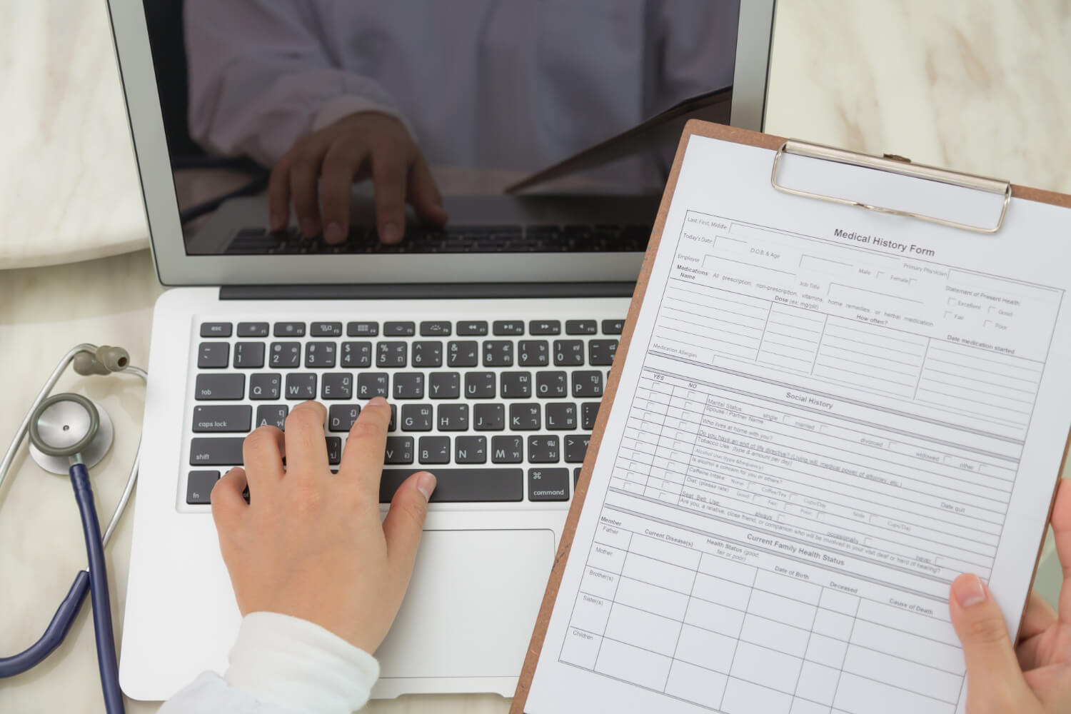 top view of doctor using a laptop and a clipboard