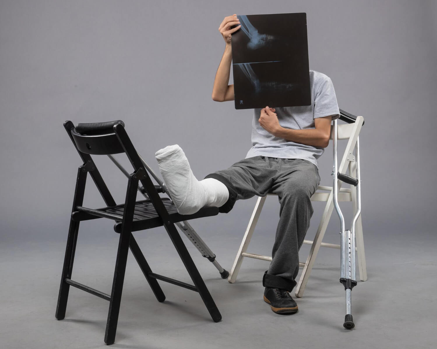 front view young male sitting with broken foot and holding x-ray of it 