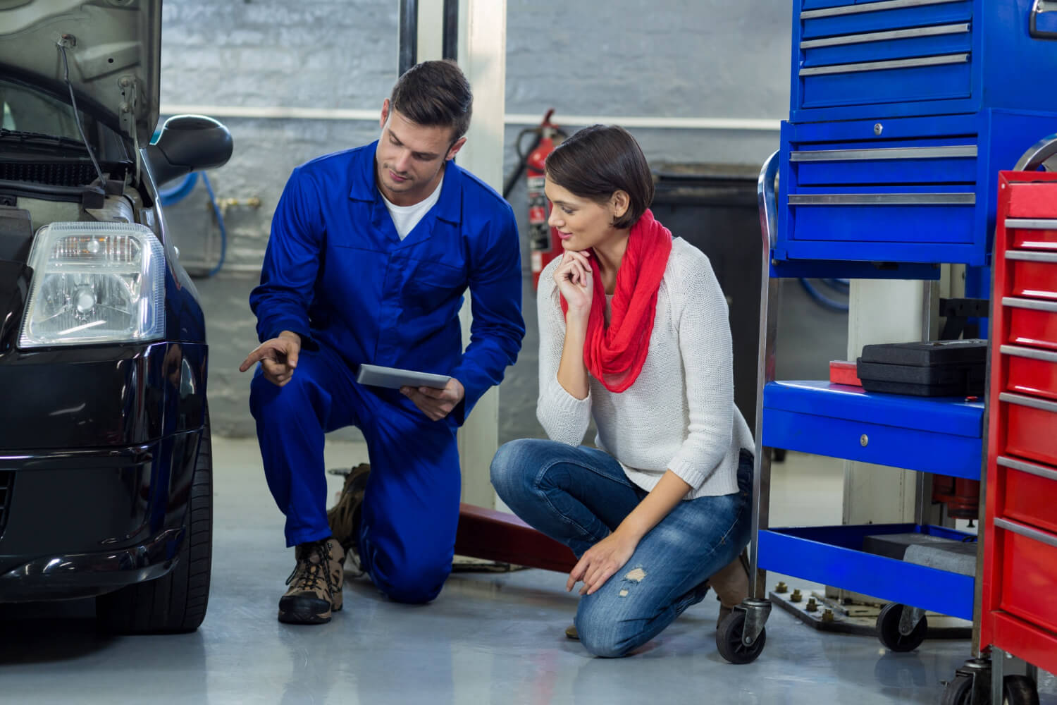 Expert mechanic showing a problem to female driver.