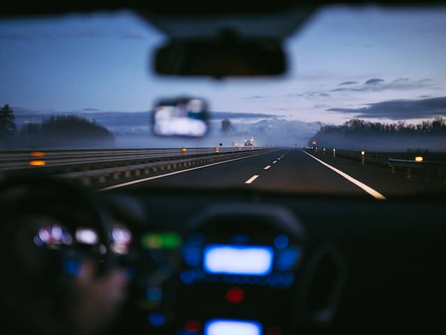 Coche circulando por una larga carretera recta al atardecer. 