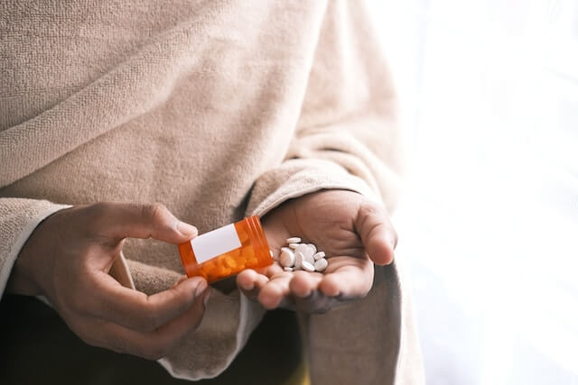 Mujer vertiendo pastillas analgésicas sobre su mano 