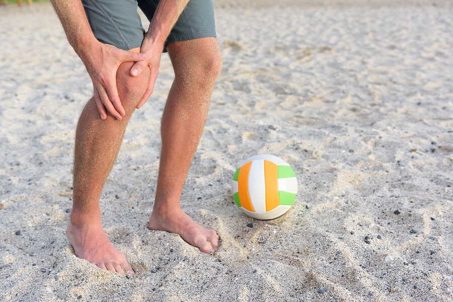 Knee injury at the beach with volley ball on the ground