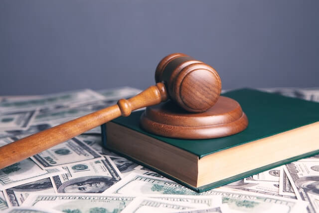 el martillo de los jueces sobre un libro verde en una mesa llena de dólares