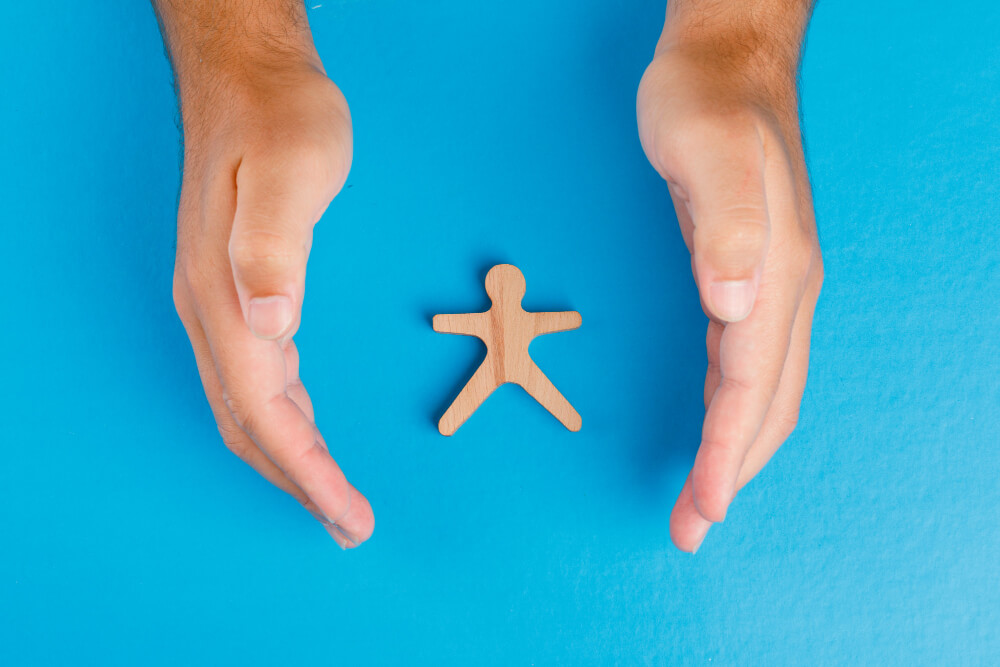 social protection concept blue table flat lay hands taking care wooden human figure