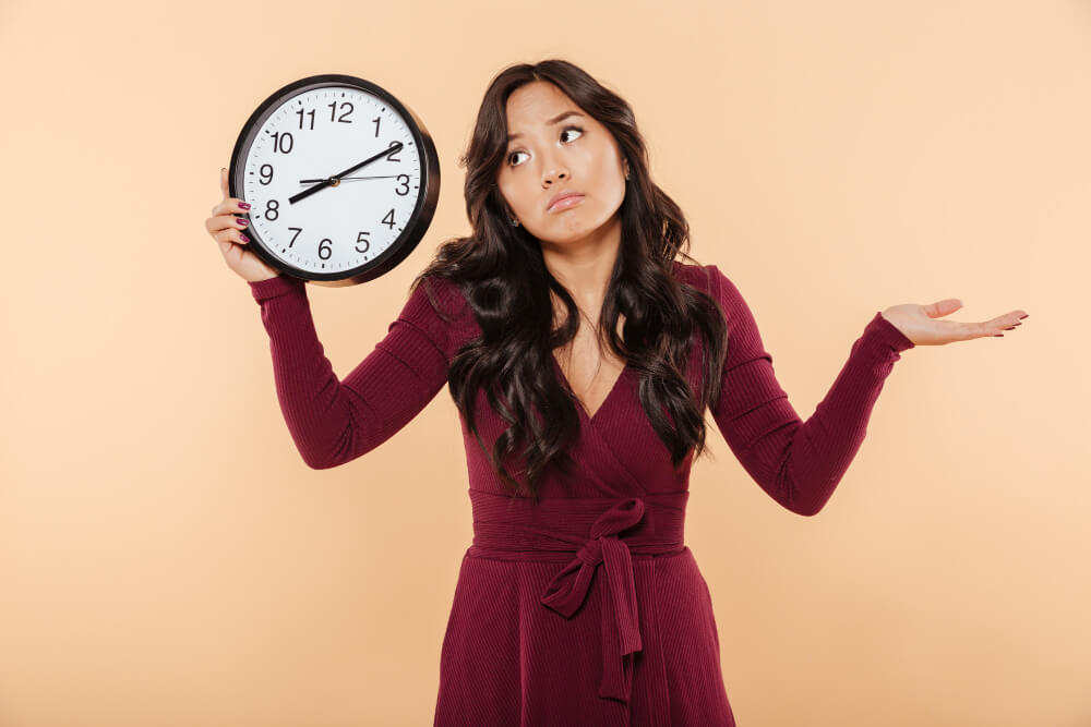 Woman holding a clock wondering how long 