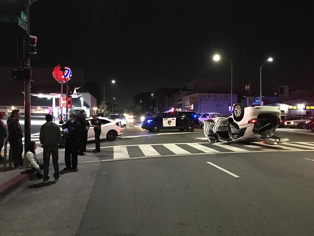 Escena de accidente de coche con transeúntes, policía y víctimas comunicándose. 
