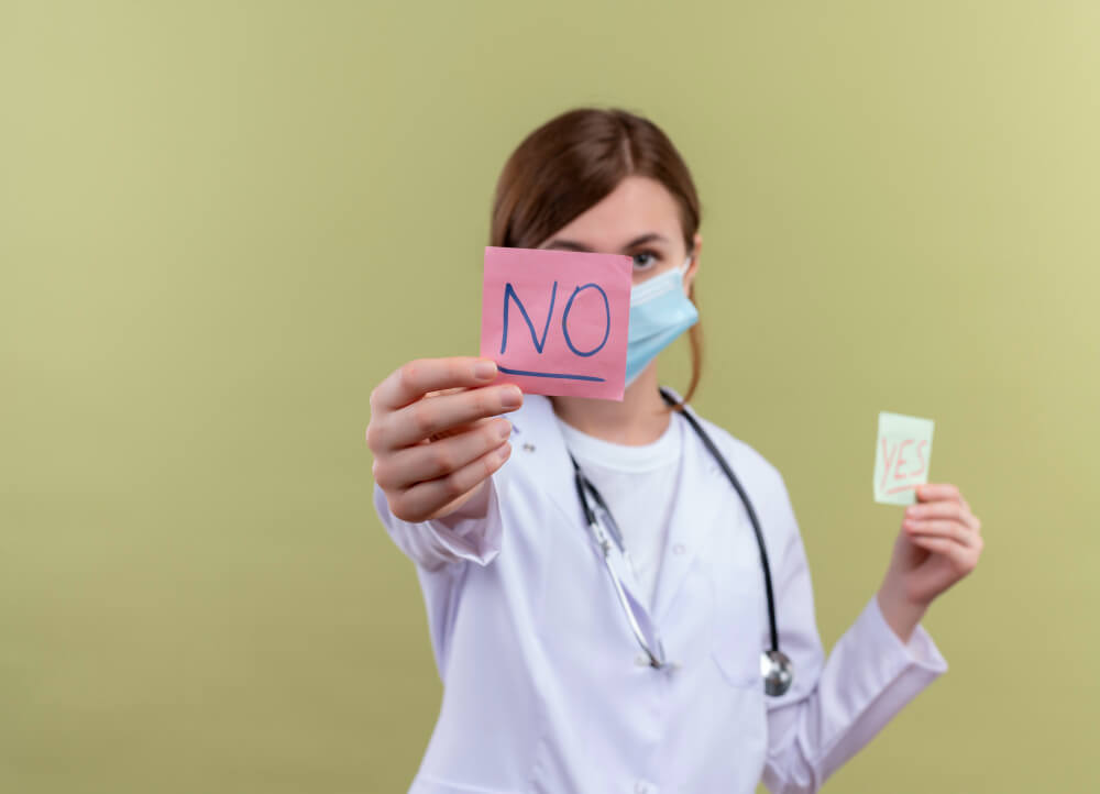 Mujer médico sosteniendo una nota adhesiva con las palabras "no". 