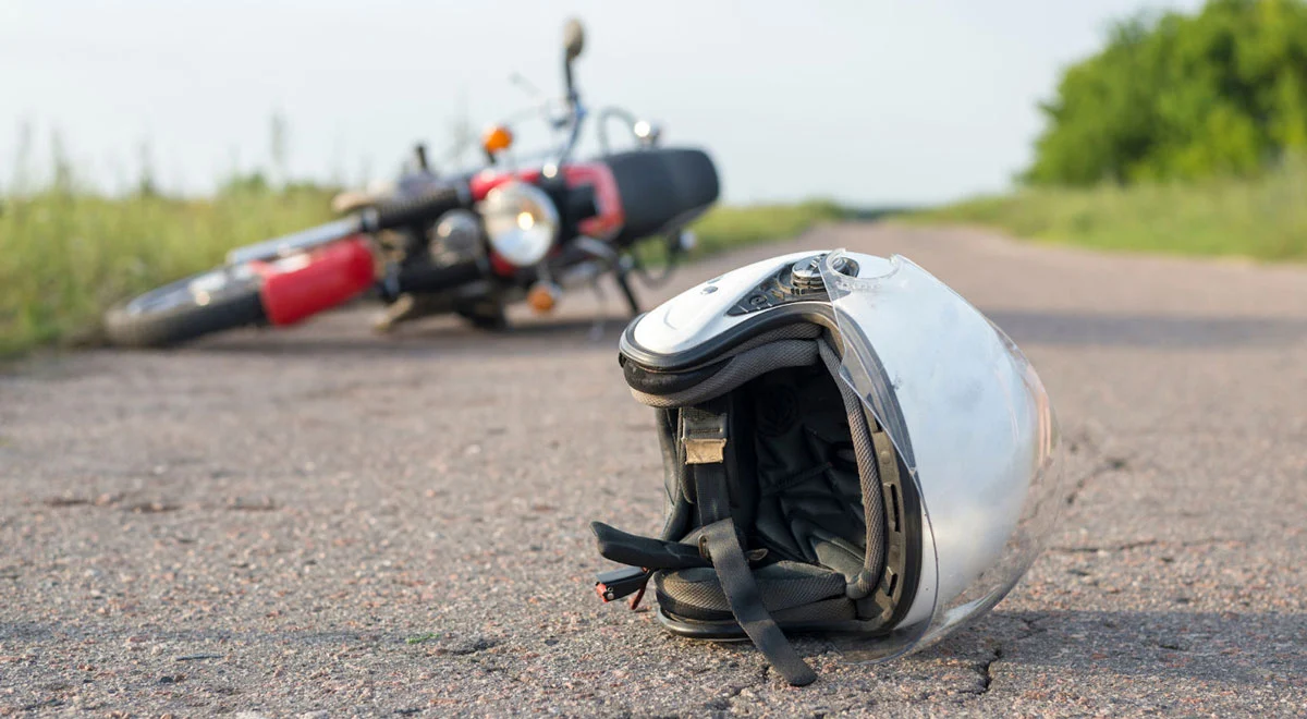 Damaged helmet laying on the concrete with a fallen motorcycle on the background after an accident.