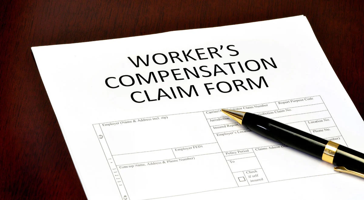 Workers' Compensation Claim form documents with pen sitting on top.