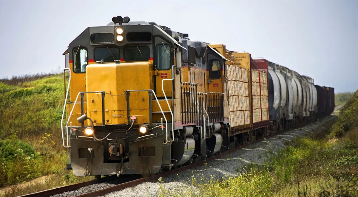 Big yellow train over some track in a small valley.