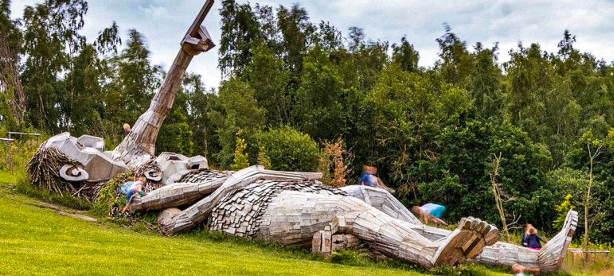 Two wooden troll sculptures lying down on the grass in De Schorre park, Antwerp