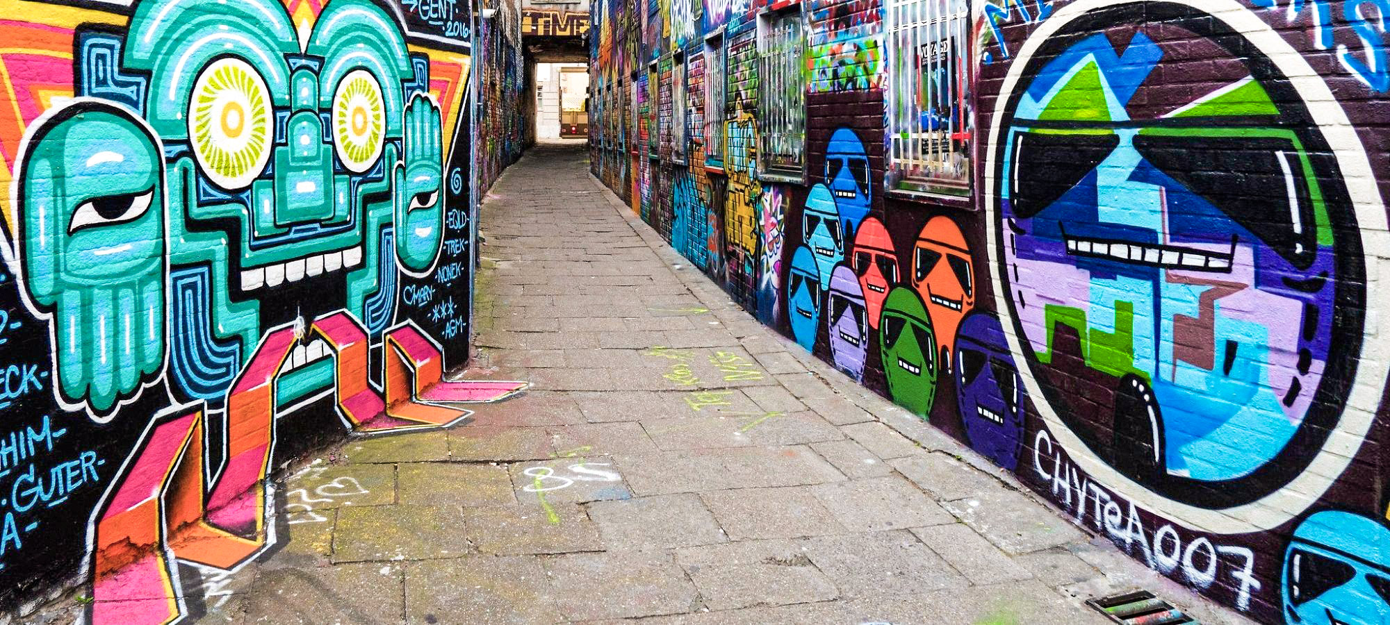 Colourful, futuristic graffiti is painted along the side of the walls of a thin alley