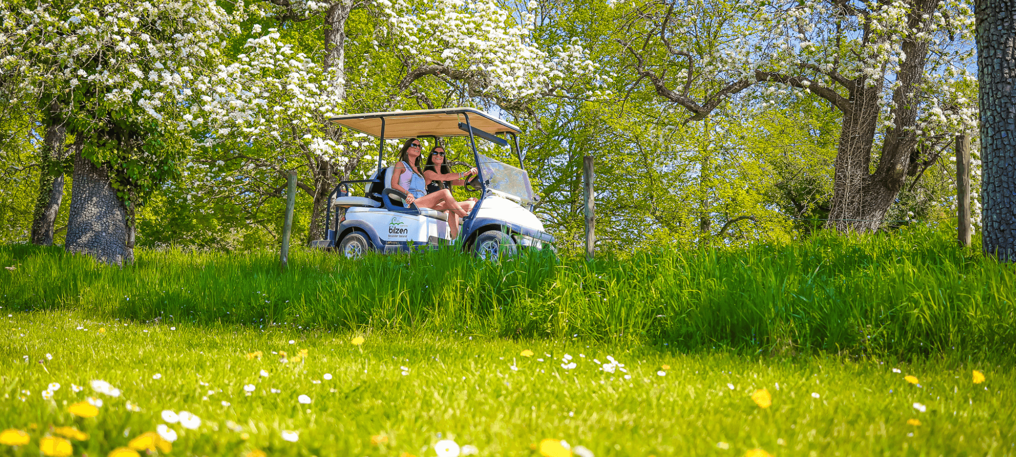 Two women riding an electric golf cart in the Belgian countryside
