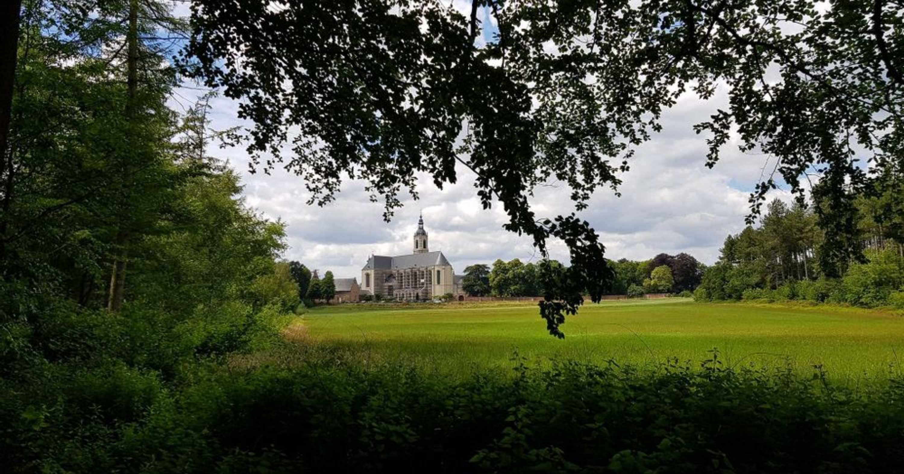 A large abbey on the other side of a field from a viewpoint in the forest in Averbode, Belgium
