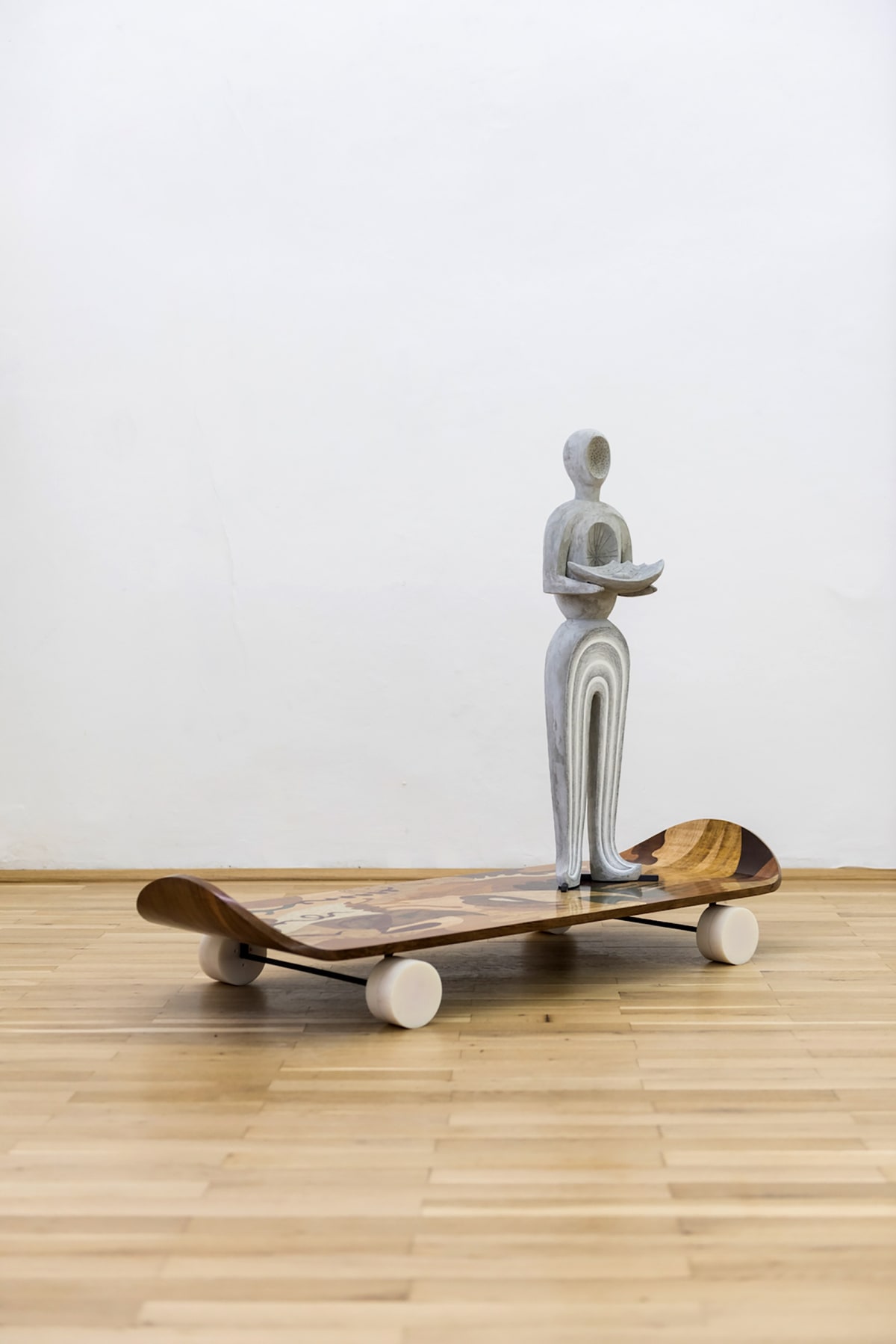 Image shows a sculpture standing on a wooden skateboard