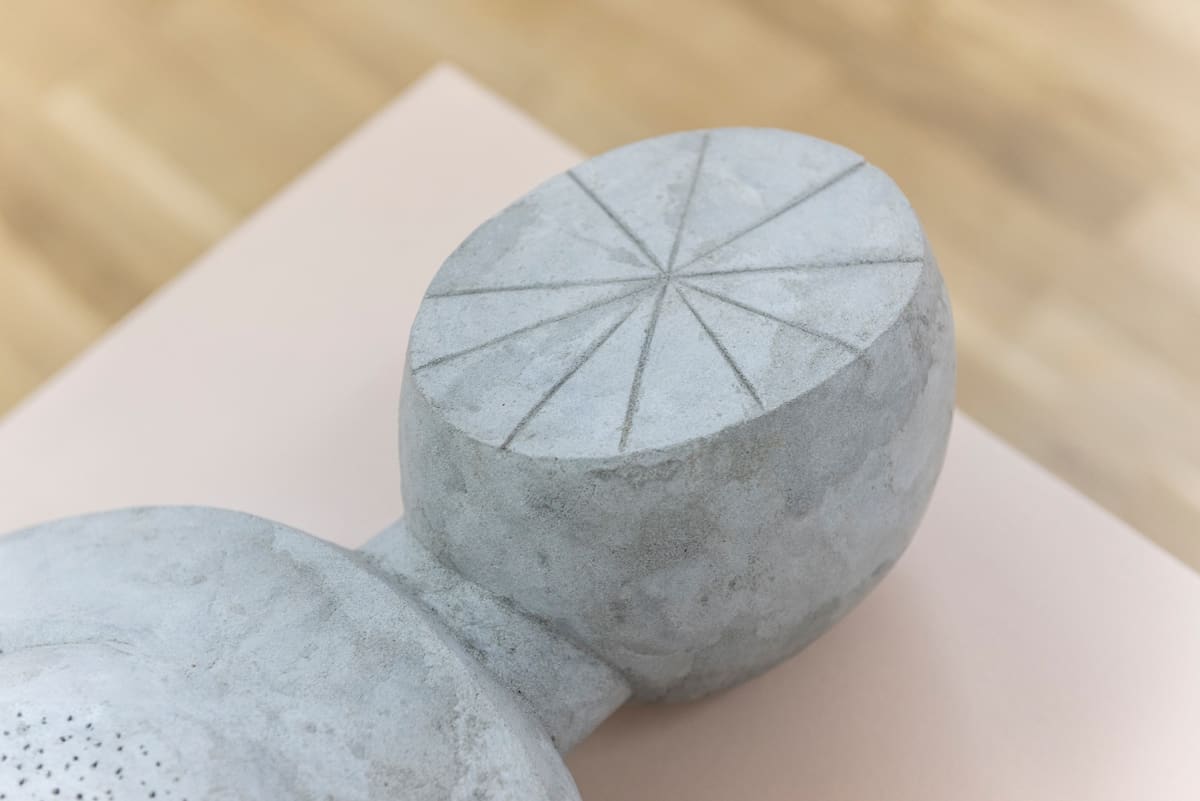 Image shows close up of the flat round head of a sculpture, where the face should be there is a star-like form made of lines coming from the center.