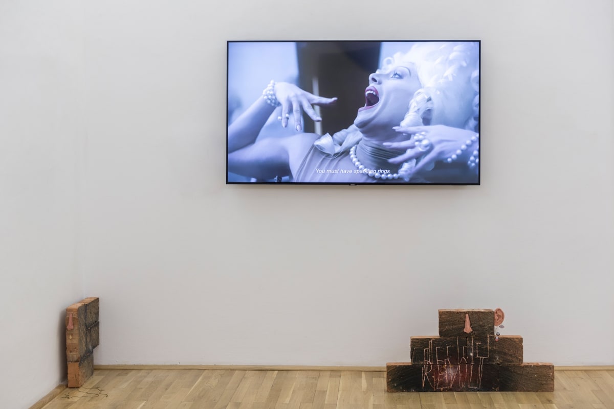 Image shows a video installation as well as 2 smaller brick sculptures on the floor