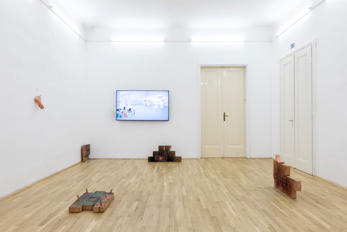Image show a room filled with art from different artists, sculptures on the floor and a foot sculpture on the wall as well as a video installation.