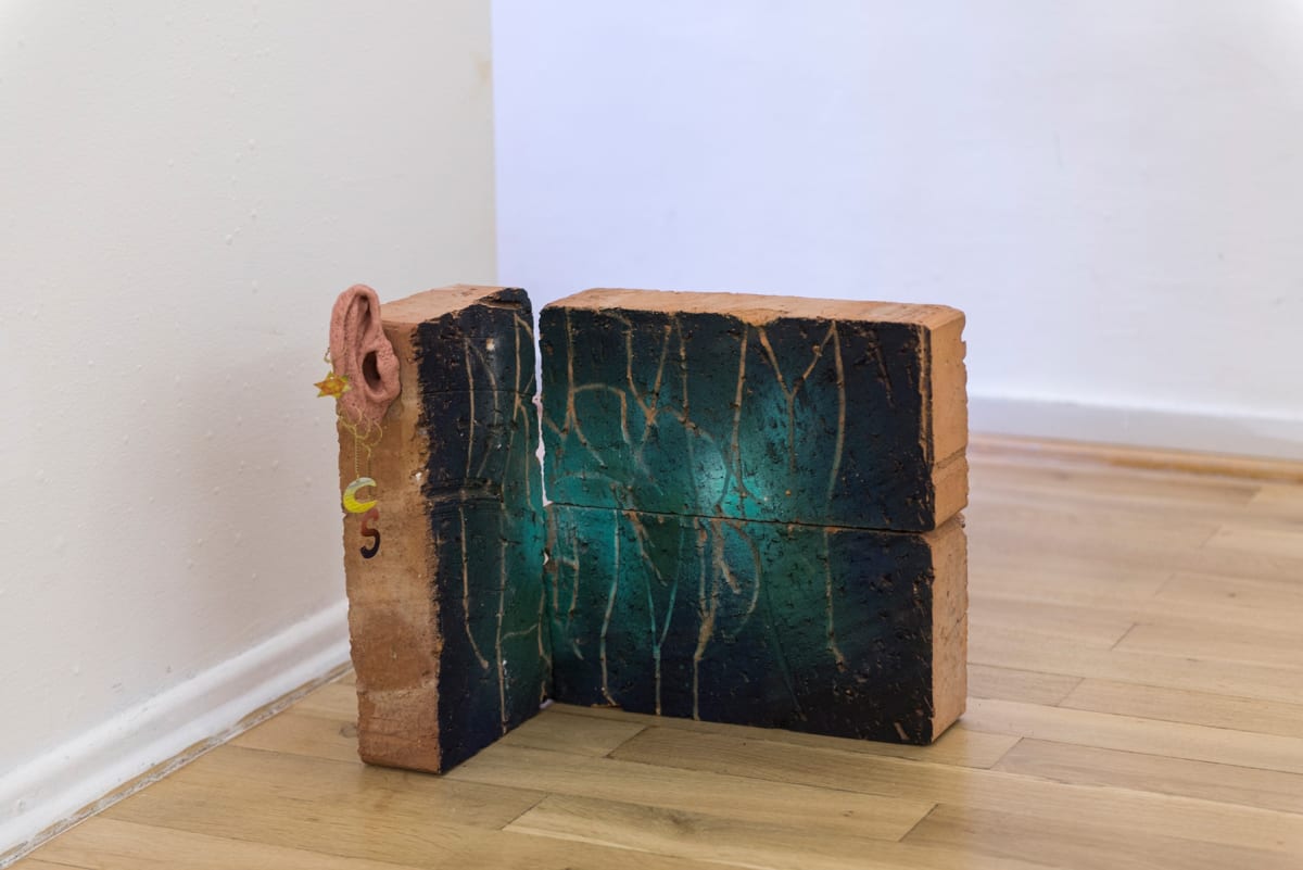 Image of a sculpture. Bricks painted on in a very dark green color and scratches on the surface
