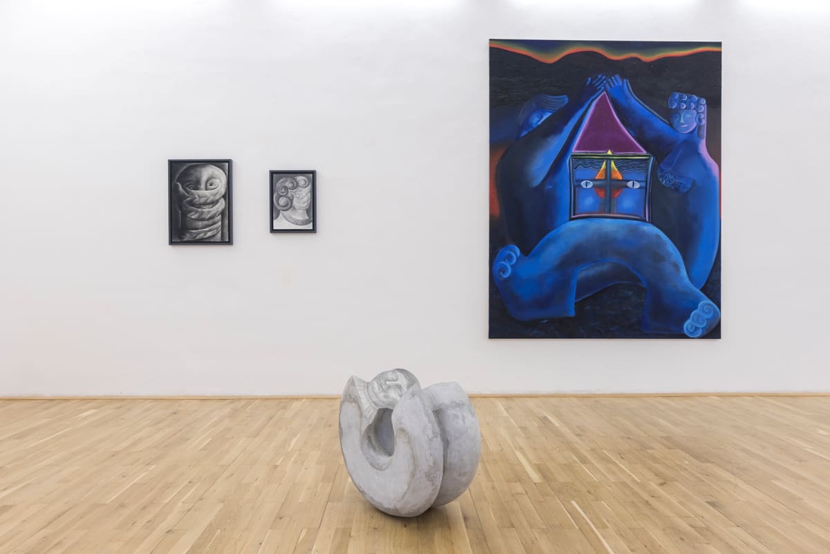 View of a room with a large blue painting, two smaller black and white drawings and a stone sculpture on the floor
