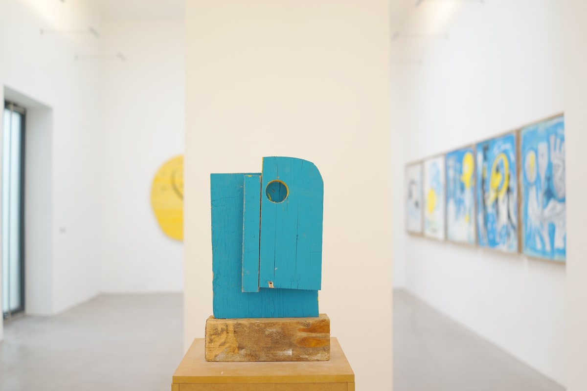 ernst koslitsch raum mit licht exhibition showing the venue artworks and a blue wooden sculpture on wooden unpainted blocks.
