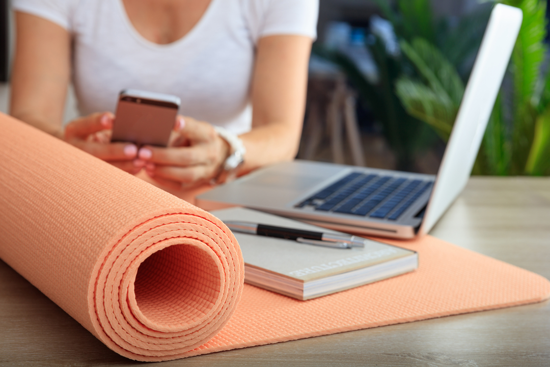 Yoga business owner sitting at her desk with pen-paper, laptop and a rolled up yoga mat