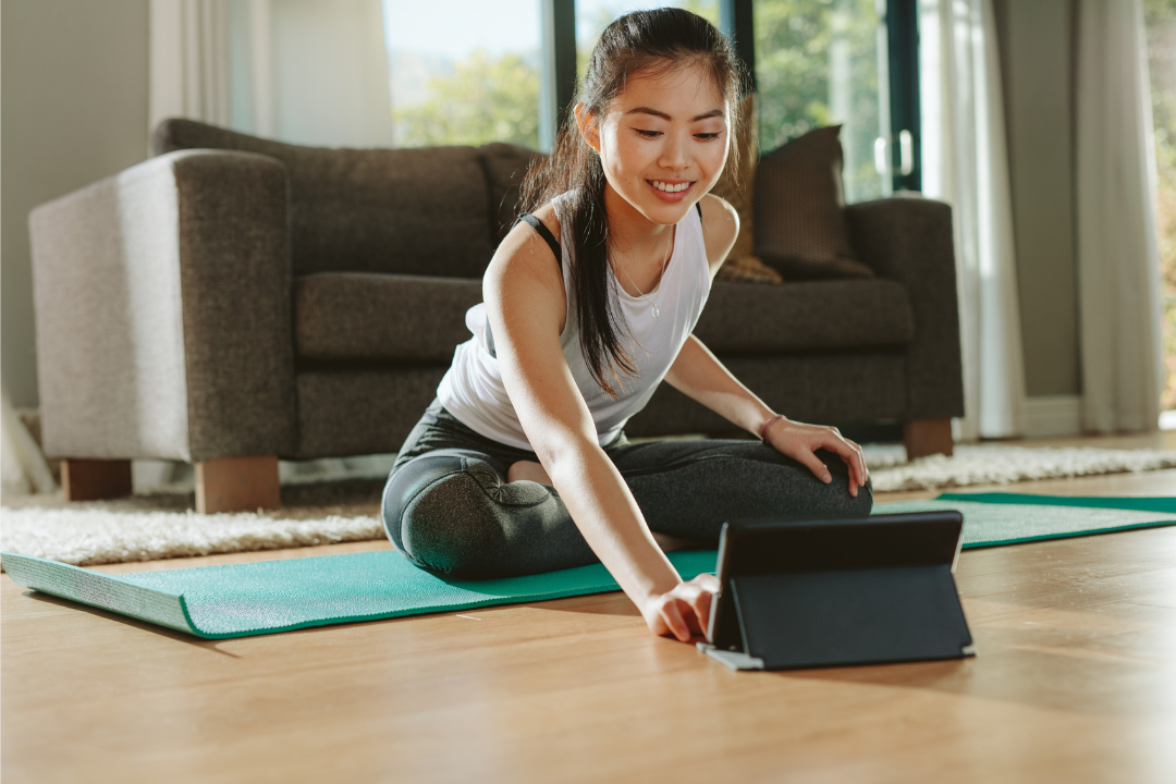 Women touching her i-pad to join a yoga class while sitting on her yoga mat