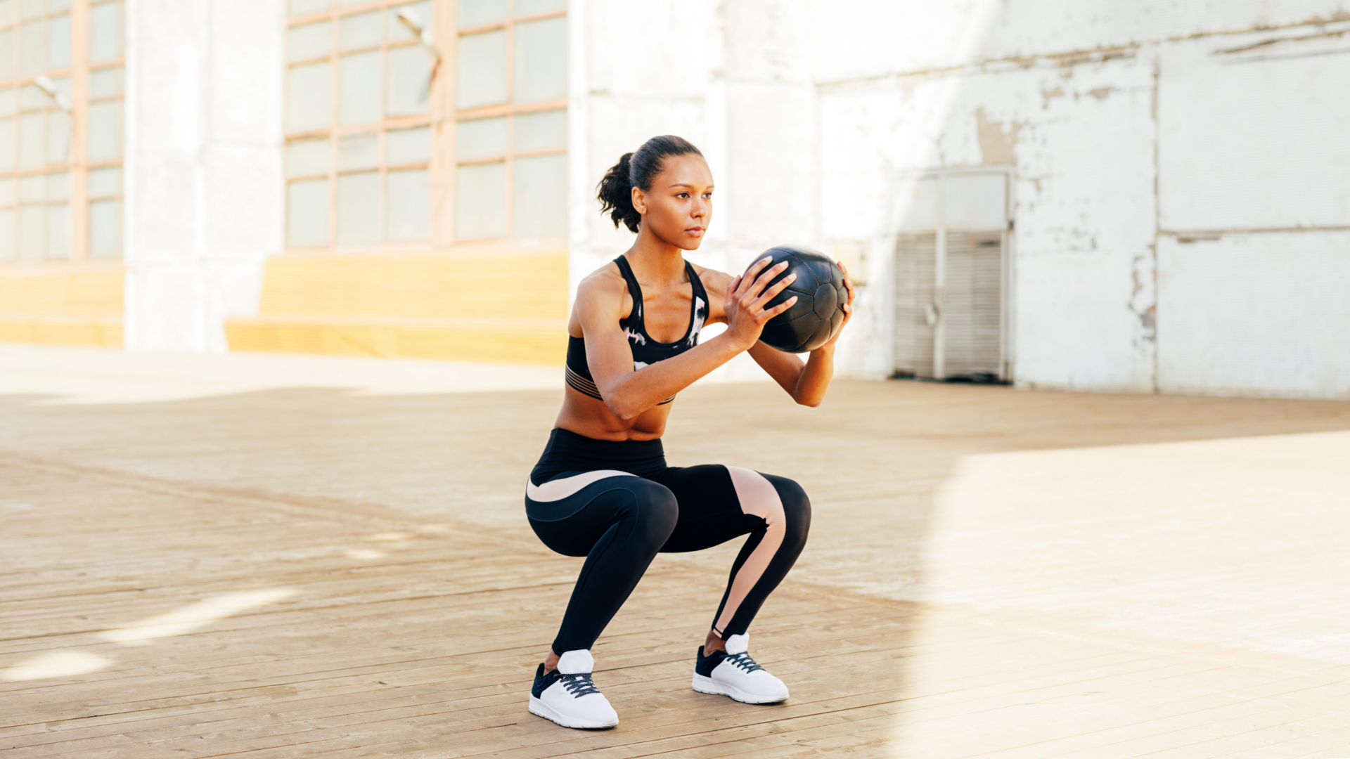 Athletic woman squaitting mid-way with a medicine ball