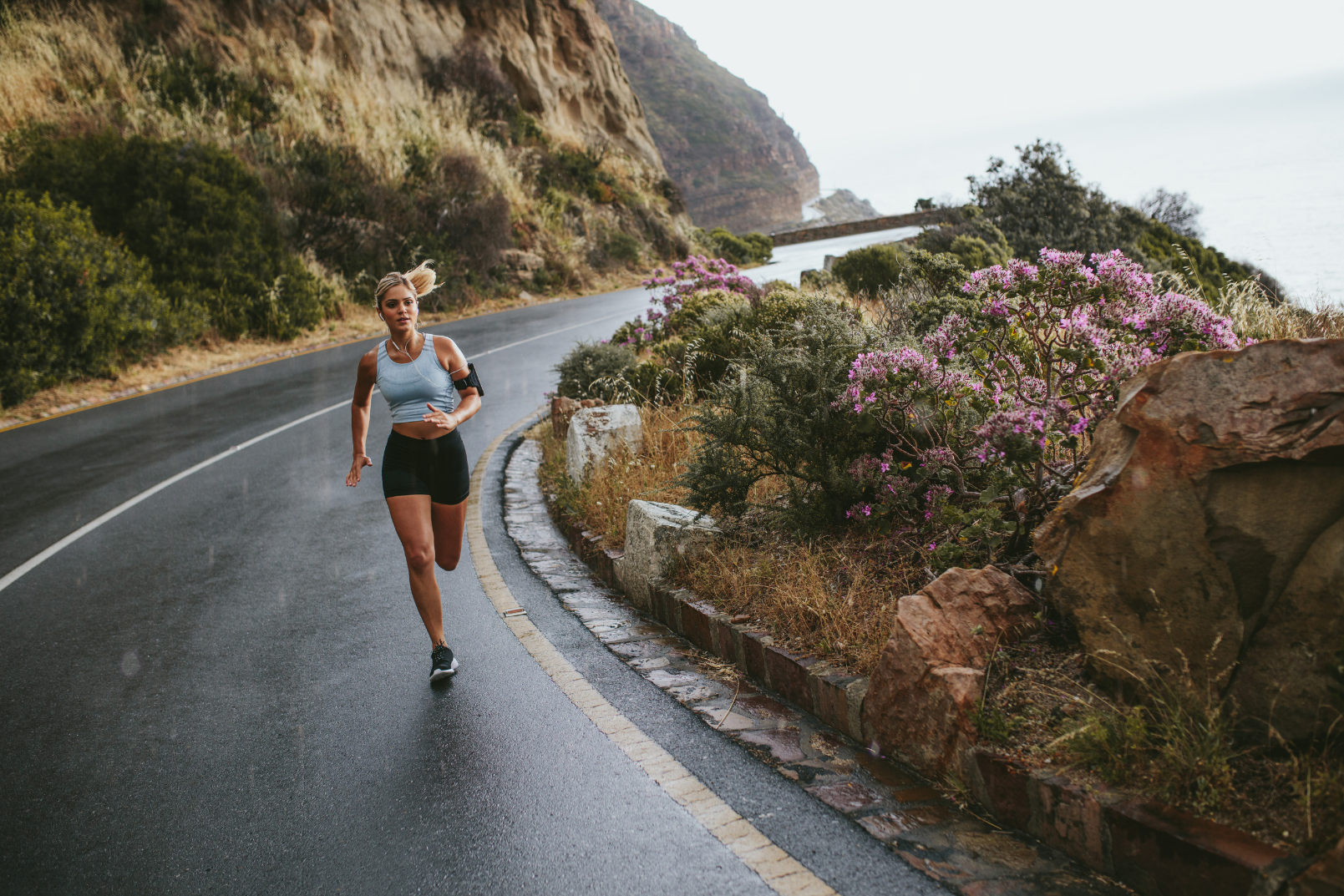 Fit woman running on an empty road besides a mountain trail
