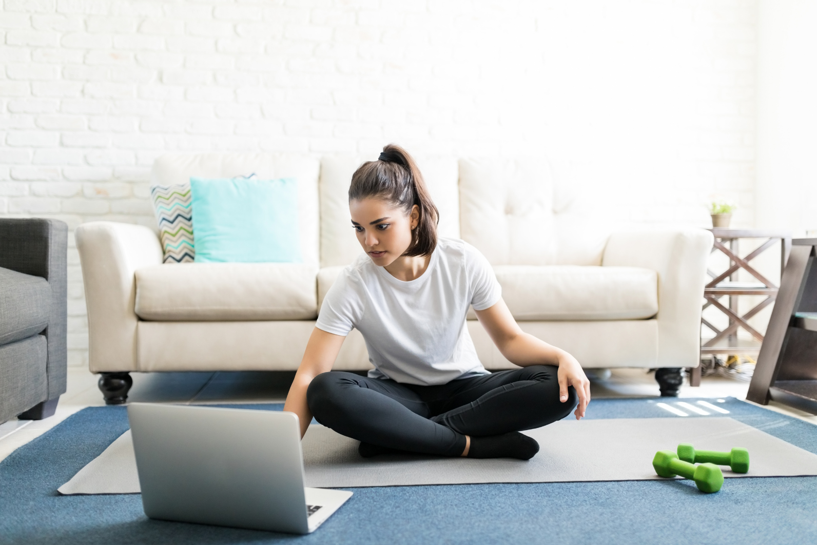 Woman sitting besides a laptop with light weights by her side
