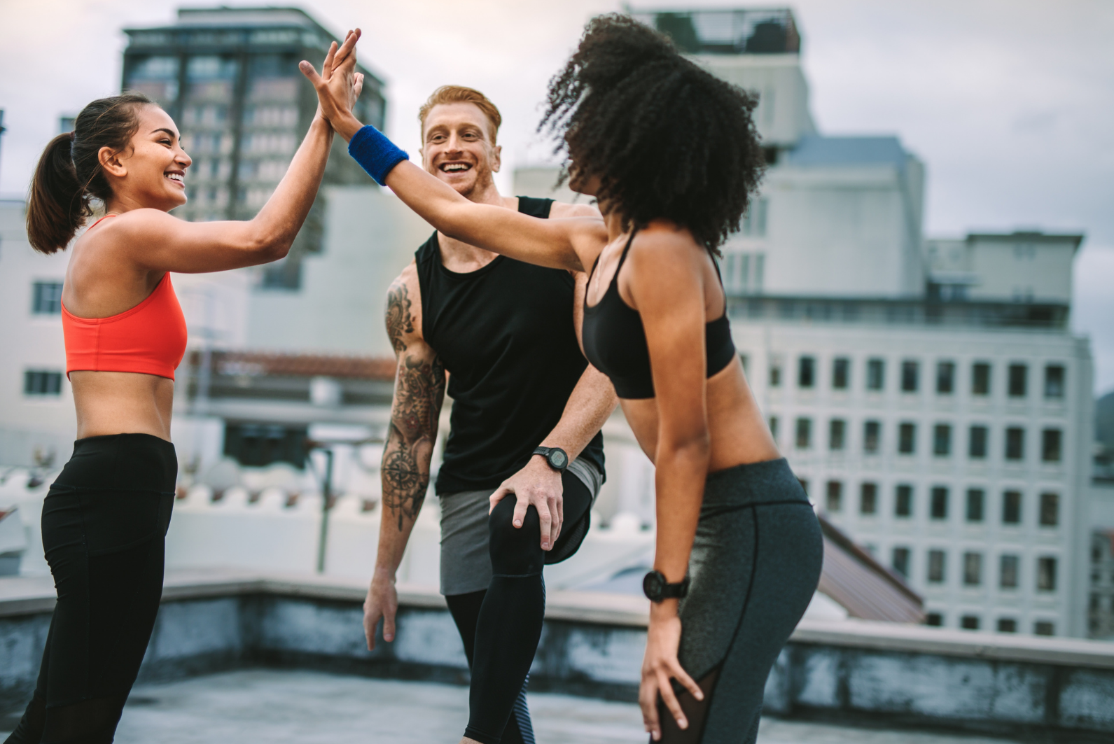 Two gym going women hi-fiving each other and a male gym goer looking at them smiling
