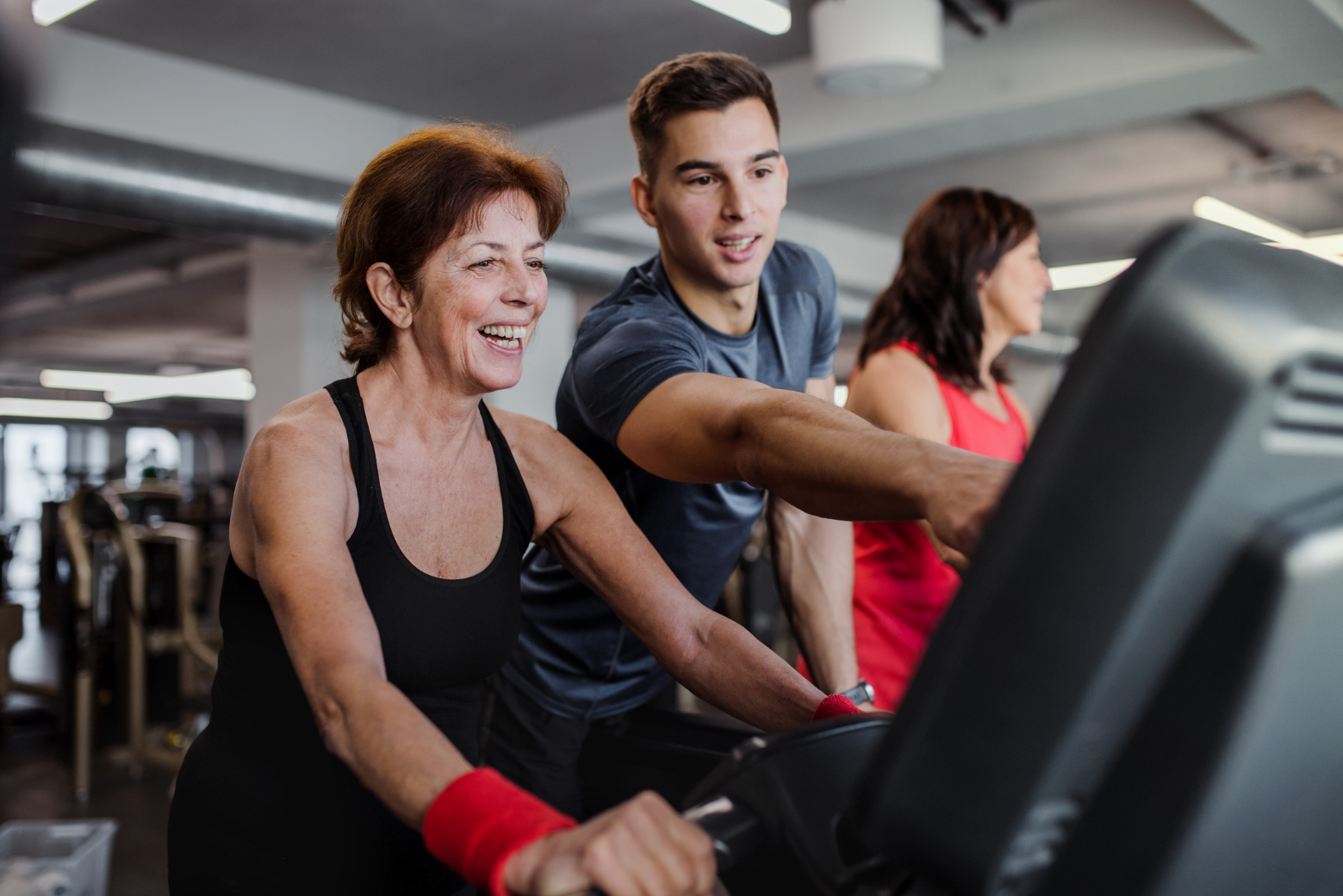 A young male fitness instructor guiding a senior citiA young male fitness instructor guiding a senior citizen woman as she cycles on a gym spin-cyclezen woman as she cycles on a gym spin-cycle