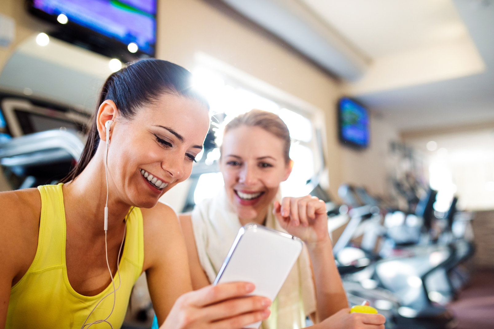 Two ladies sitting in a gym and watching a video on their mobile phone