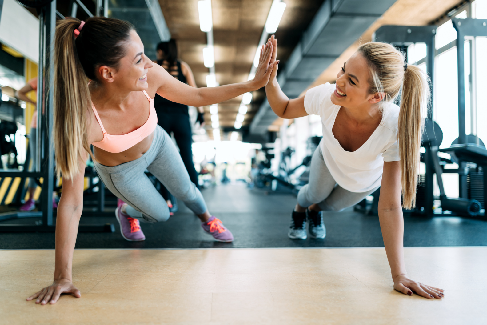Two fit women hi-fiving each other with one hand in push up position