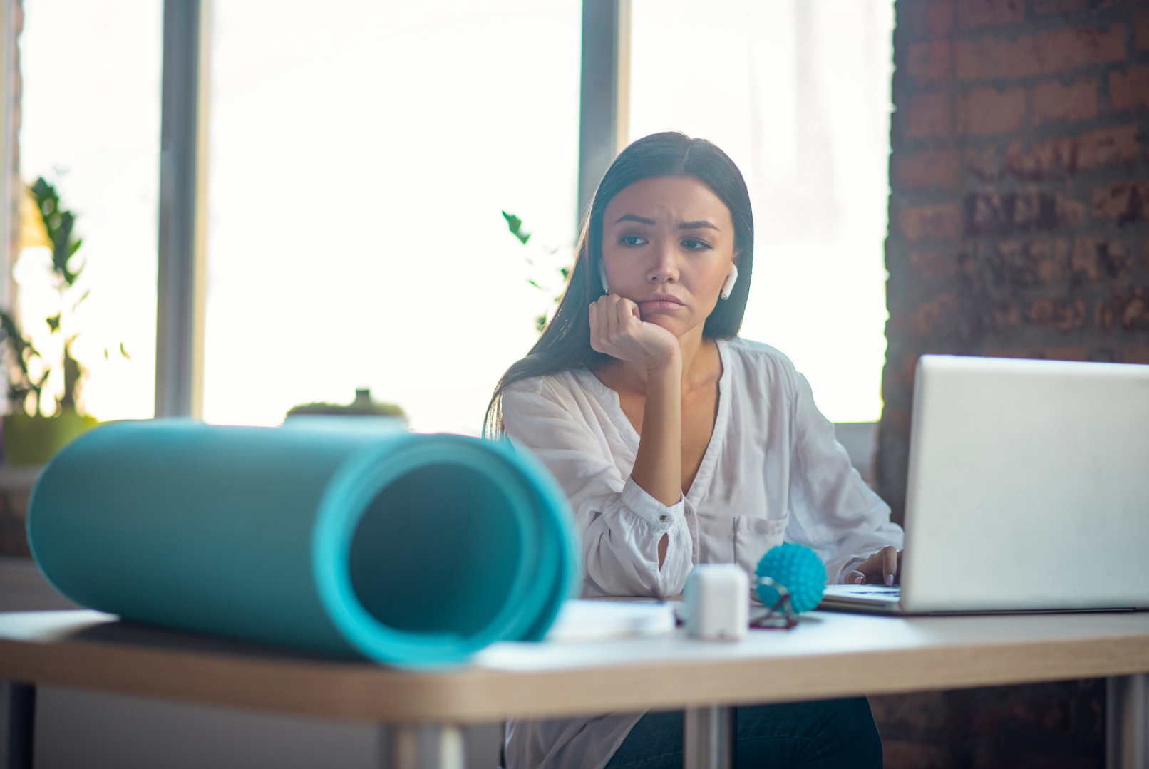 Sad woman sitting with a laptop and a yog mat.