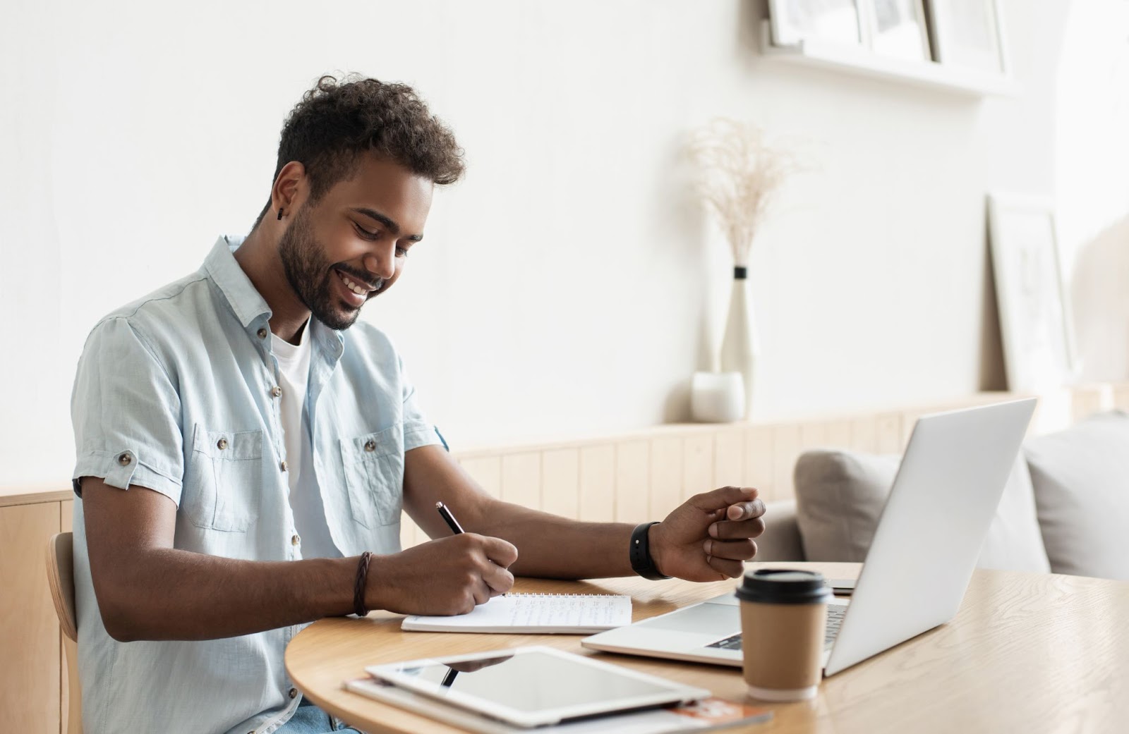 SaaS marketing: Smiling man writing on his notebook with his laptop in front of him