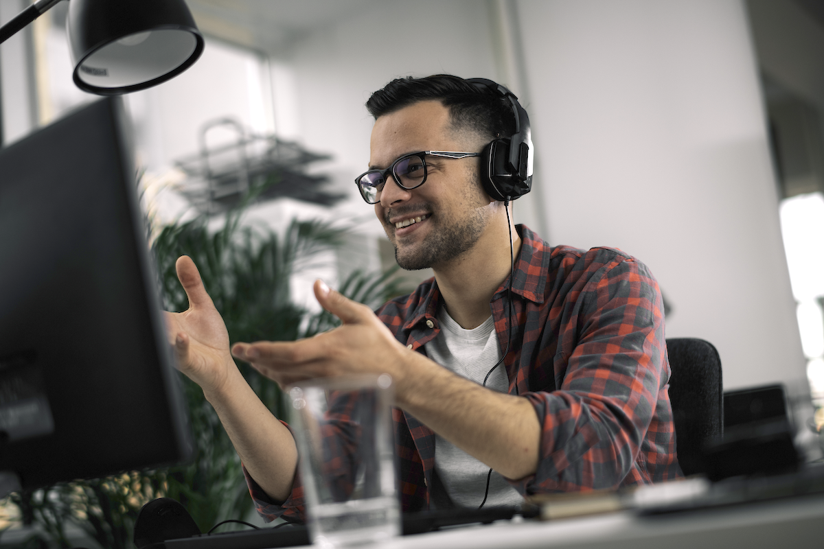 sales enablement app: Smiling man wearing headphones on and doing hand gestures in front of his computer