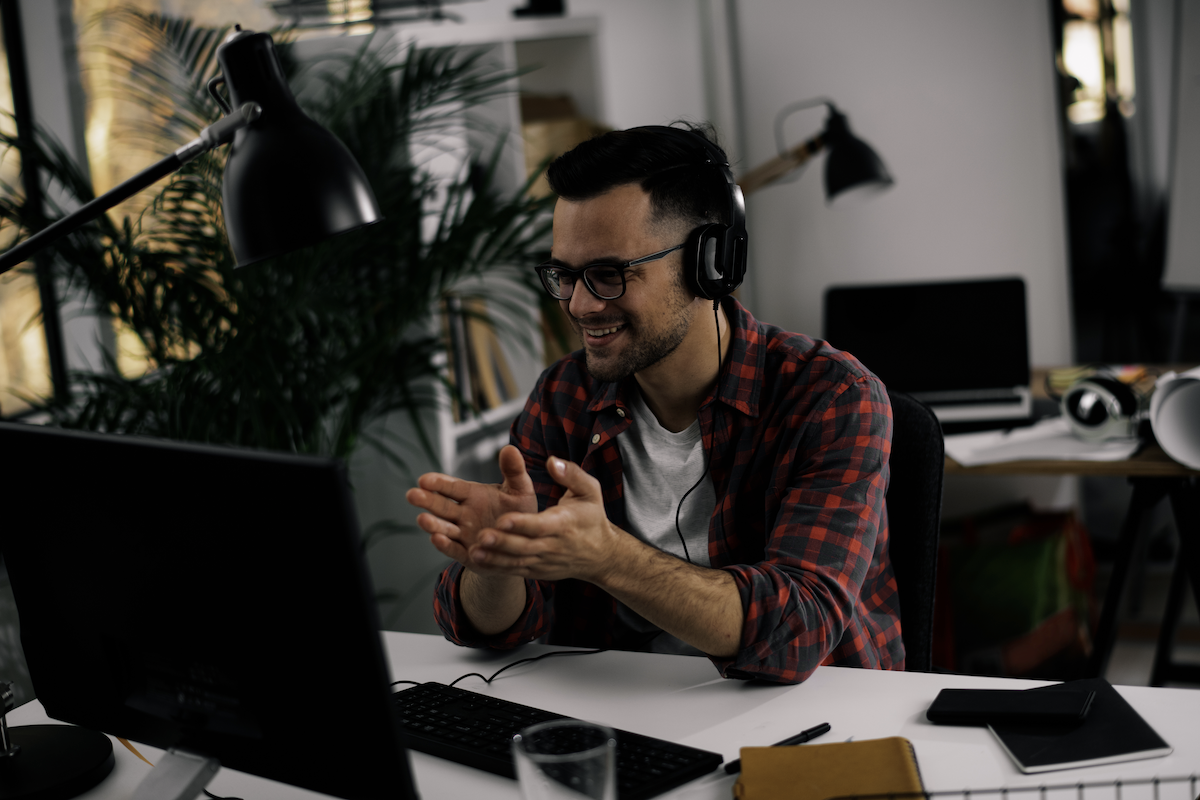 growth marketing: Smiling man talking to someone on his laptop while wearing headphones