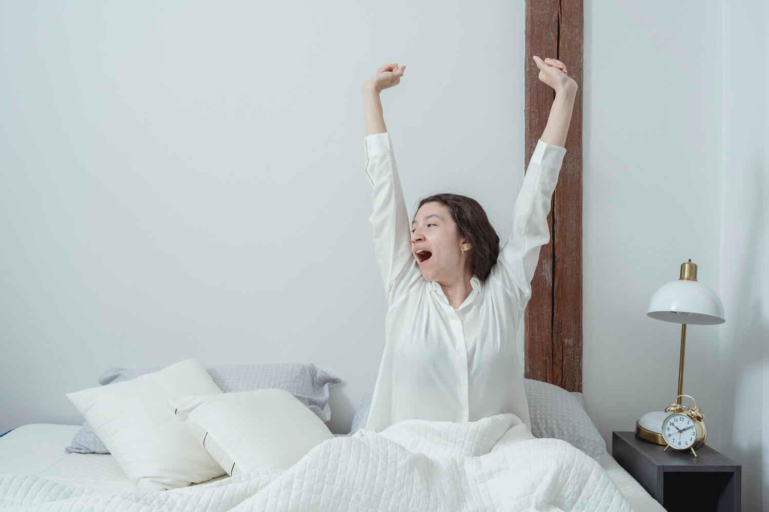 Une femme s'étire dans sont lit, en pyjama blanc.