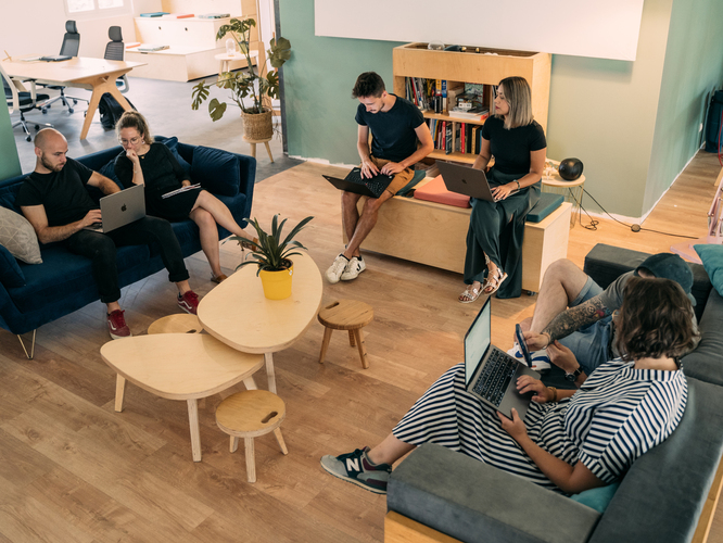 Espace détente au travail avec deux canapés, deux tables basses en bois ainsi que des plantes et une bibliothèque.