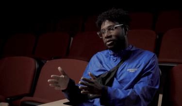 Screenshot of a black man talking with his hands up explaining.
