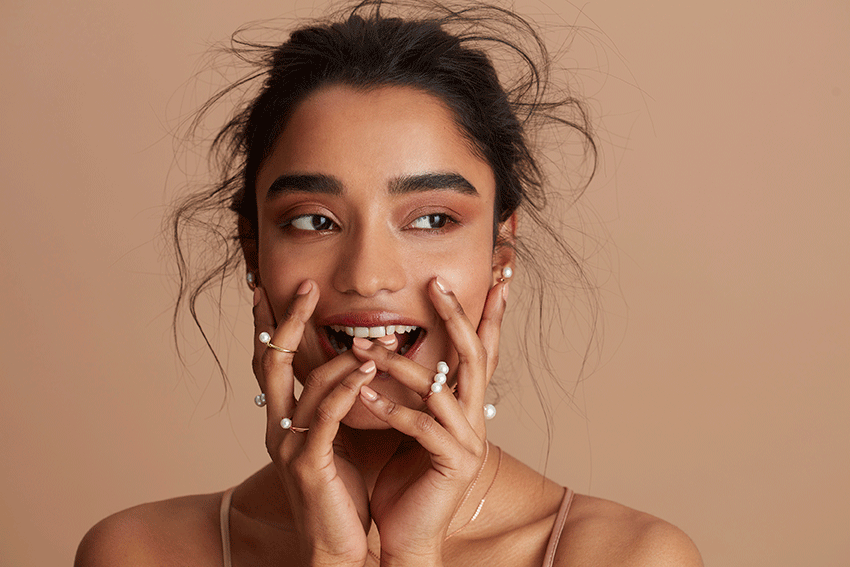 Close up of the face and hands of a smiling model wearing pearl rings and earrings created by Olivia & Pearl London