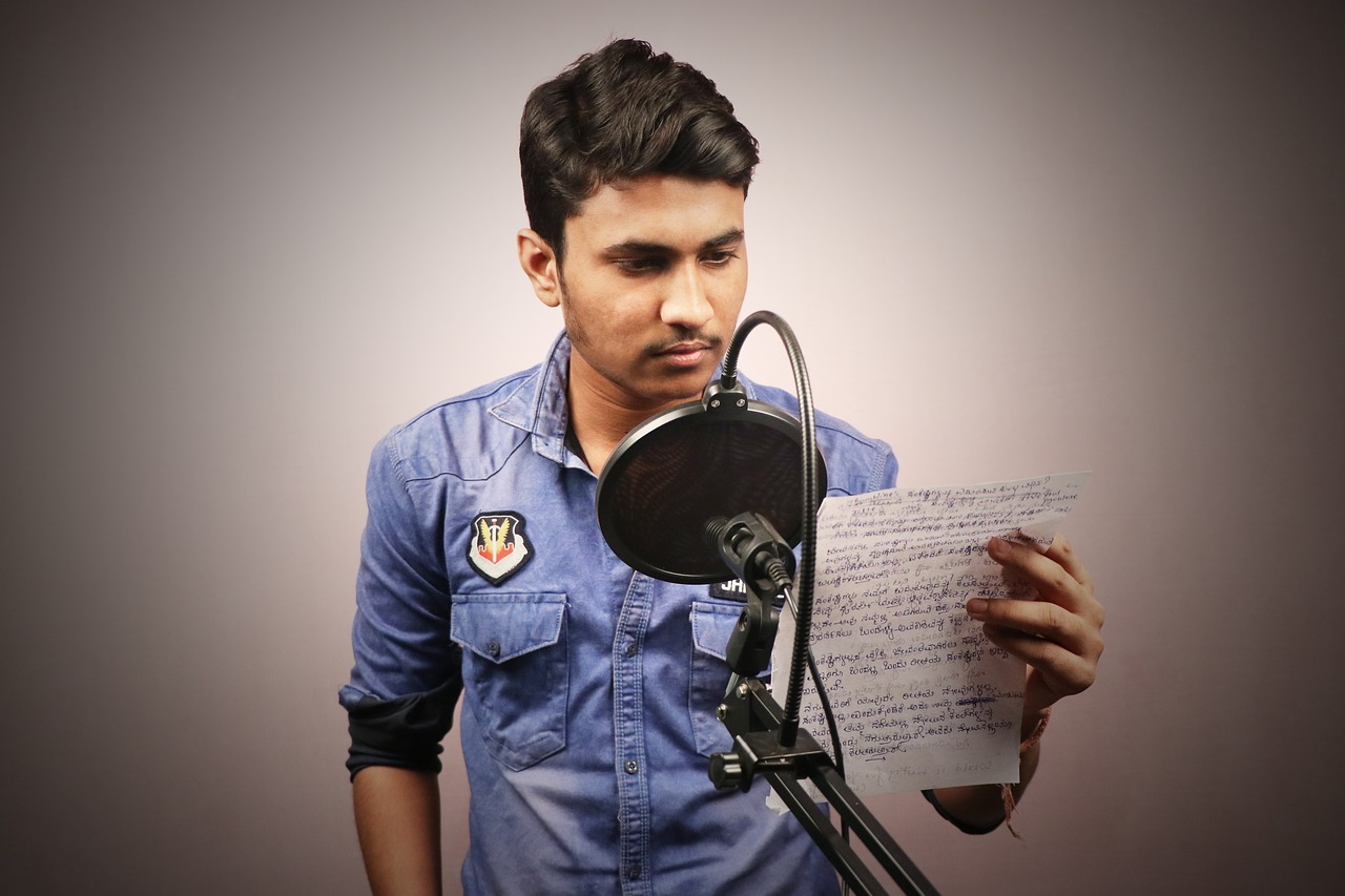 A man stands in front of a microphone reading a script