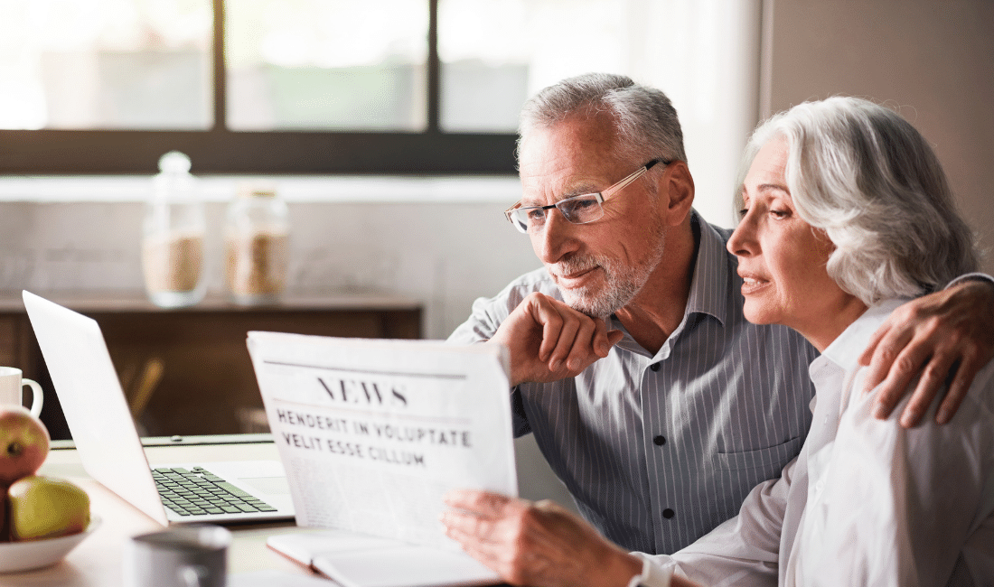 Happy and caring old couple reading newspaper at the kitchen