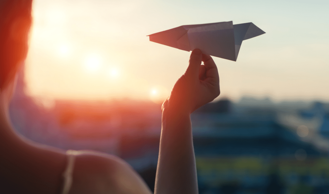 A girl is launching a paper airplane from a window