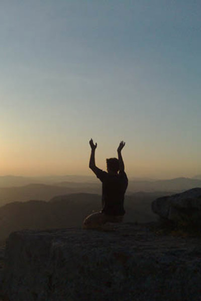 man practicing yoga on a mountian top facing the sun