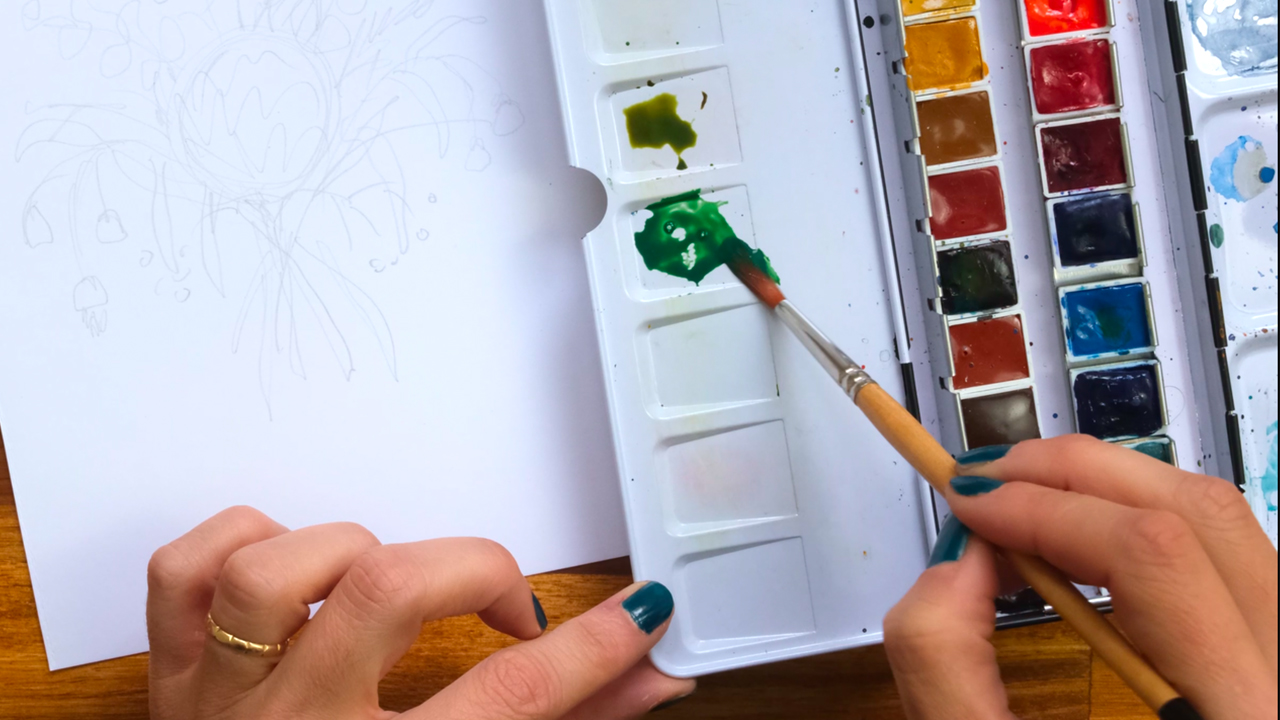 Artist's hand mixing green watercolours