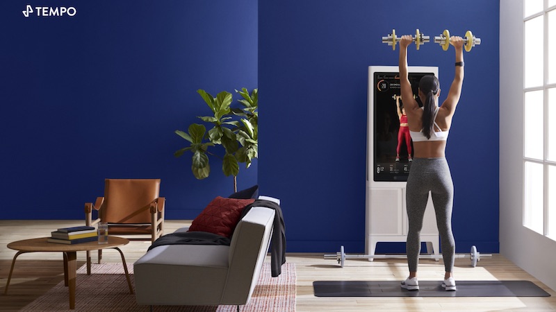 A woman lifting weights while working out in front of the Tonal home gym.