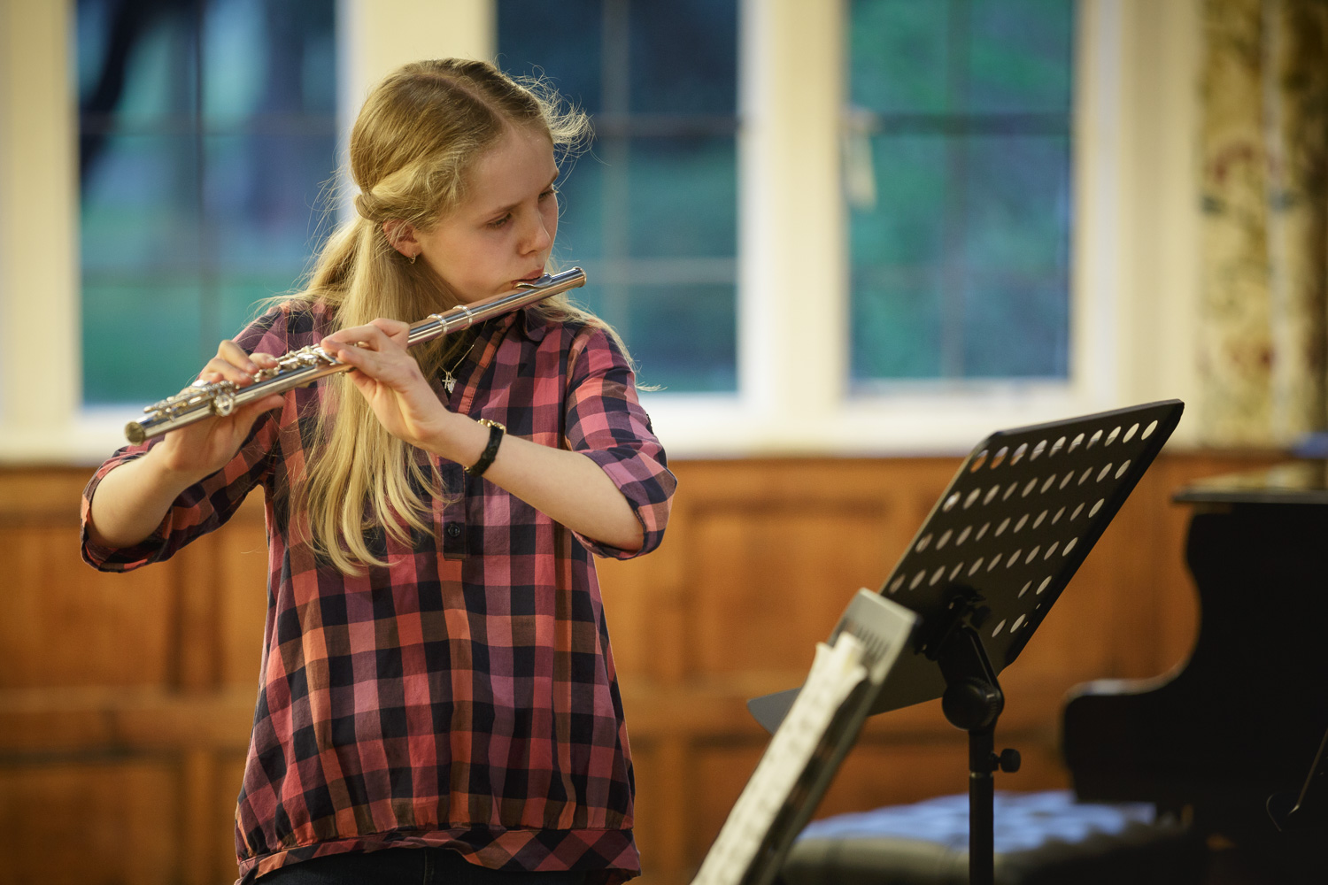 A child with long blond hair plays the flute.