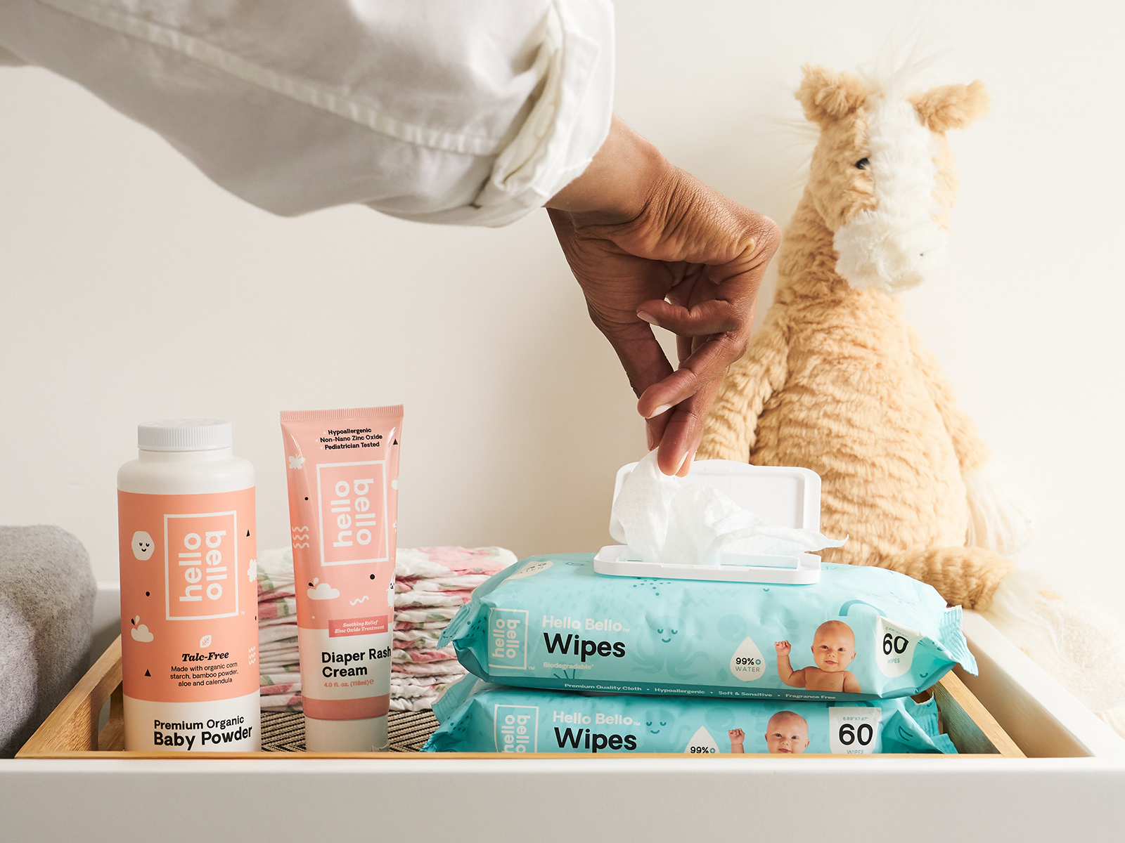 Hello Bello lifestyle image of a person opening a container of baby wipes. Featuring baby wipes, diaper rash cream, and baby powder.